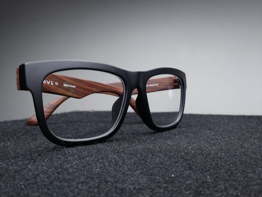 pexels-photo-39716 Close-up of fashionable black and wooden frame glasses on dark fabric with a soft-focus background.