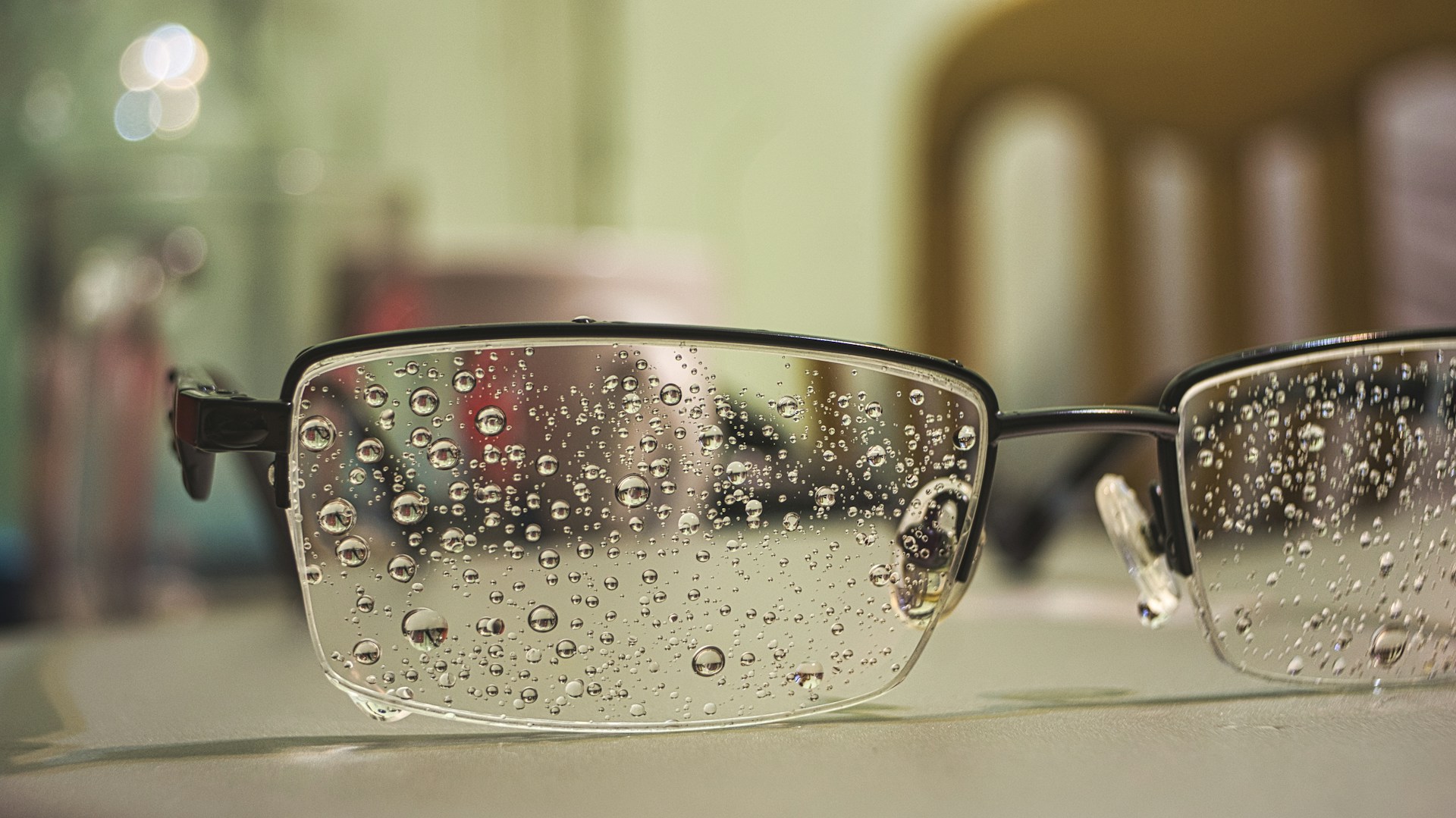 A close-up of eyeglasses covered in water droplets after being rinsed with dish soap, showing the lens cleaning process.